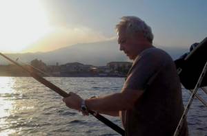 Fisherman checking the line of his fishing rod fishing. In the background Etna