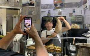 Man photographing the baker showing a loaf of bread
