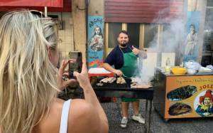 Woman photographing a man grilling meat